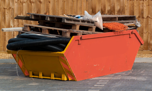 Loaded skip on a commercial site with pallets, pipe and timber