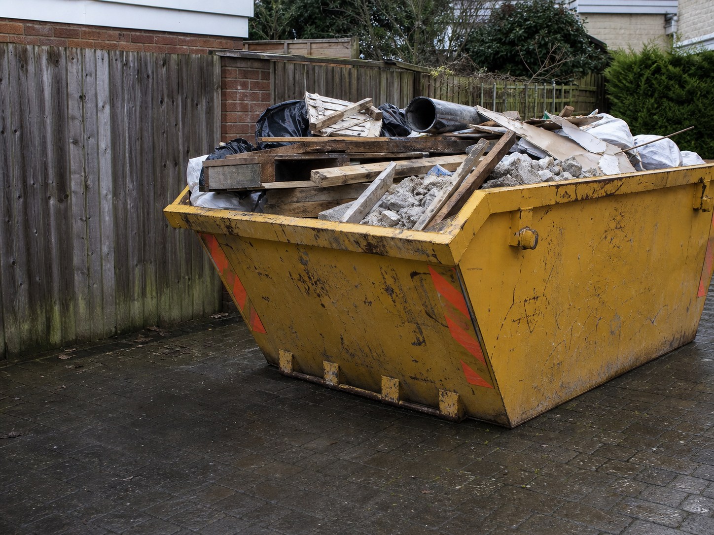 Clean yellow skip loaded with timber, rubble bags and construction waste on a paved Bristol site